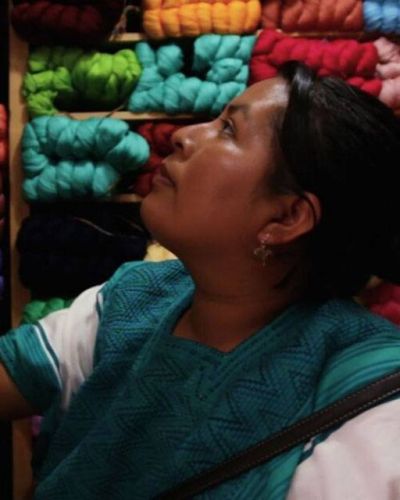 een vrouw in traditionele mexicaande kleding bekijkt een voorraad gekleurde garens